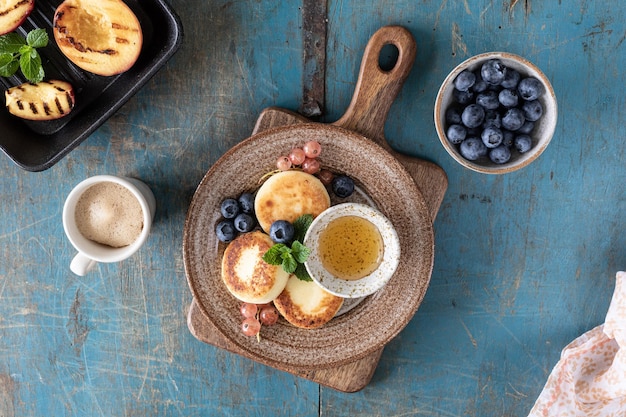 カッテージ チーズ パンケーキ チーズケーキ リコッタ チーズ フリッター新鮮なブルーベリー スグリと皿の上の桃 休日のための健康的でおいしい朝食 青い木製の背景