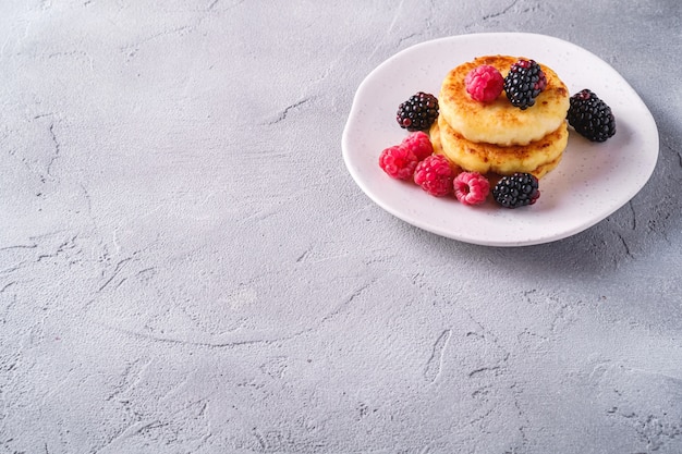 Frittelle di ricotta, frittelle di cagliata dessert con lampone e bacche di mora in lamiera su sfondo di pietra di cemento, angolo di copia spazio