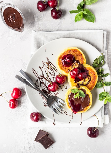 Cottage cheese pancakes or fritters with chocolate and cherry jam, fresh cherry and mint. Traditional Ukrainian and Russian cuisine. Healthy and diet breakfast.