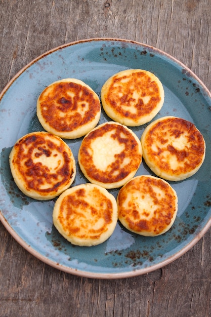 Photo cottage cheese pancakes or syrniki  on blue plate, closeup view. russian, ukrainian cuisine. healthy tasty breakfast. top view.