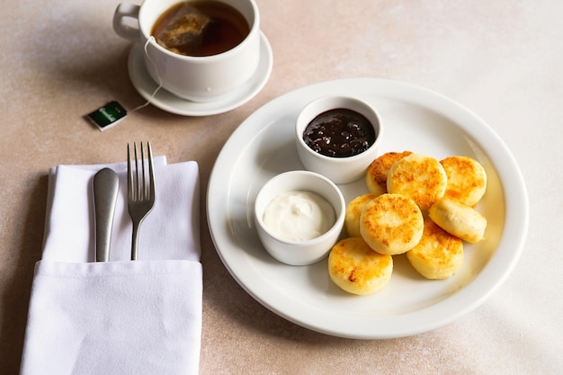 Frittelle di ricotta frittelle di ricotta syrniki su piastra in ceramica bianca con panna acida e marmellata colazione mattutina sana e deliziosa sfondo beige cibo per bambini