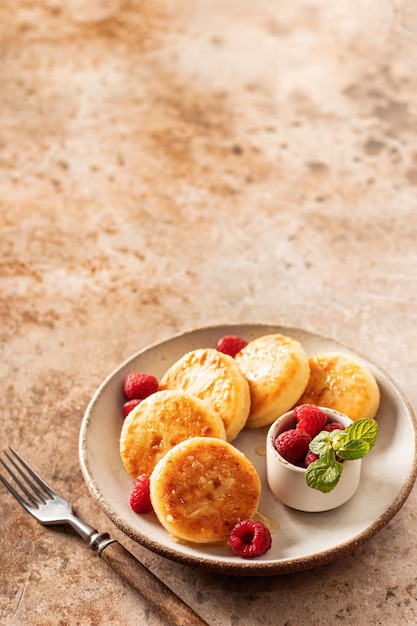 Foto frittelle di ricotta syrniki con topping al miele e lampone e menta su piatto in ceramica con forchetta su sfondo testurizzato spazio di testo