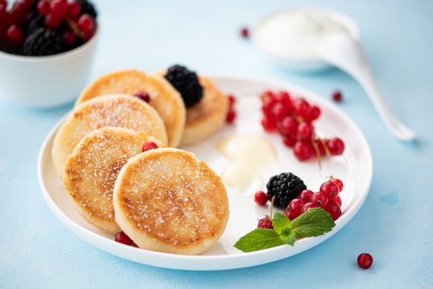 Foto frittelle di ricotta con frutti di bosco e panna acida su un tavolo blu