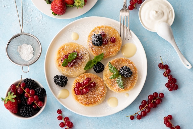 Frittelle di ricotta con frutti di bosco e panna acida su un tavolo blu