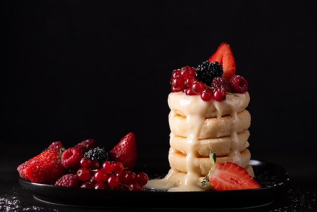 Cottage cheese pancakes with fresh berries and condensed milk on a black dish