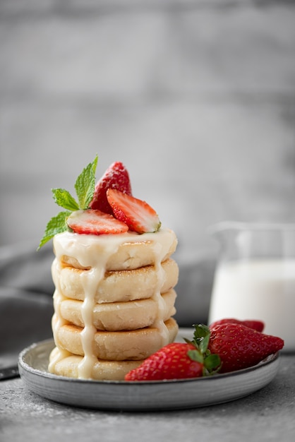 Cottage cheese pancakes with fresh strawberries, mint and milk on a gray plate