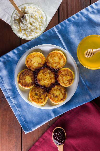 Cottage cheese pancakes with jam on a white plate Pancakes with cottage cheese and honey on wooden background Top view