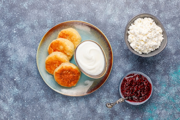 Cottage cheese pancakes with raspberry jam.Russian syrniki or sirniki, cottage cheese fritters or pancakes with a bowl of fresh homemade cottage cheese on dark grey