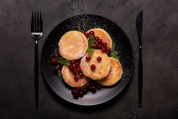 Cottage cheese pancakes with red currants, mint and powdered sugar on a black plate