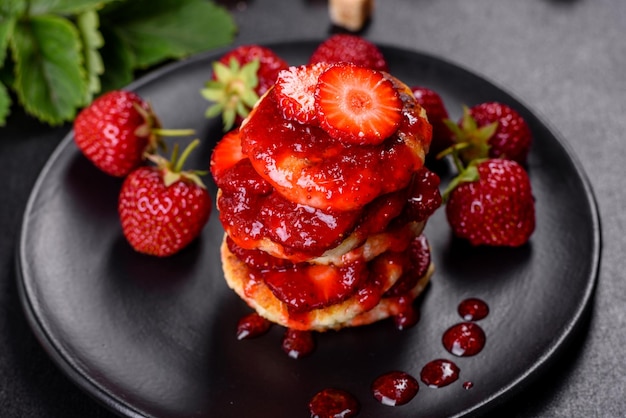 Cottage cheese pancakes with sliced strawberries and strawberry jam on a plate on a concrete background