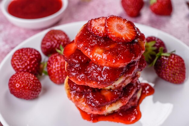 Cottage cheese pancakes with sliced strawberries and strawberry jam on a plate on a concrete background