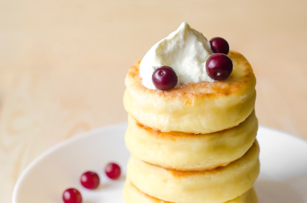 Foto frittelle di ricotta con panna acida e frutti di bosco su fondo rustico. syrniki.