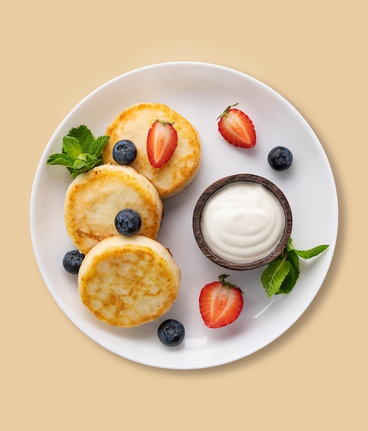 Фото Блинчики с творогом со сметаной, мятой, черникой и клубникой на желтом фоне здоровый и вкусный завтрак вид сверху
