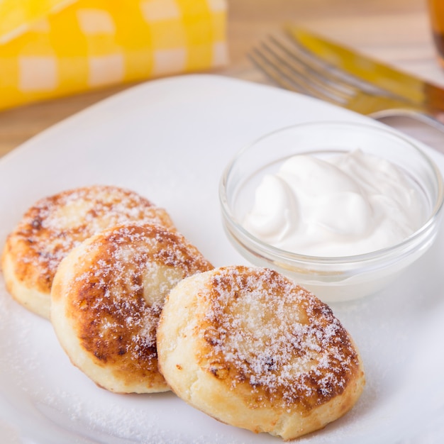 Cottage cheese pancakes with  sour cream and powdered sugar in a white plate.