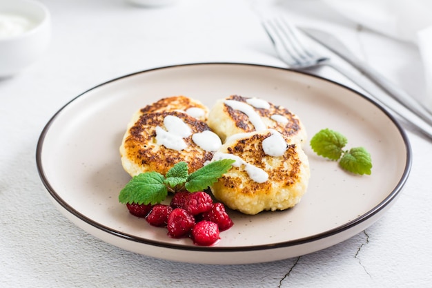 Cottage cheese pancakes with sour cream raspberries and mint on a plate on the table