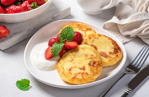 Cottage cheese pancakes with sour cream and strawberries on a light background