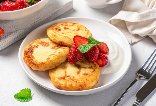 Cottage cheese pancakes with strawberries mint and sour cream in a white plate on a gray background