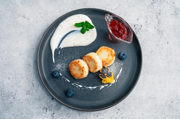 Cottage cheese pannenkoeken syrniki op bord met zure room en jam bosbes en eetbare bloemen gezondheid