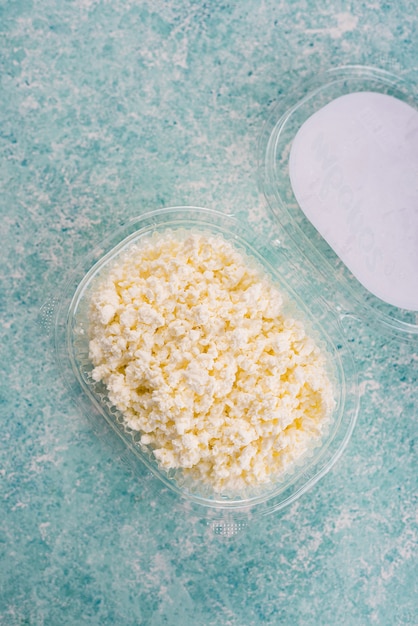 Cottage cheese in plastic packaging from a farm on a light, turquoise background.