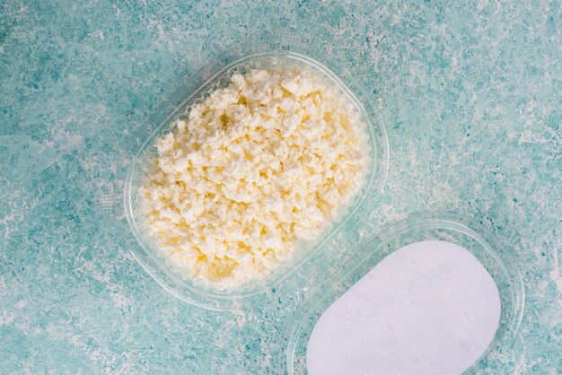 Cottage cheese in plastic packaging from a farm on a light, turquoise background.