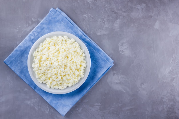 Cottage cheese in a plate. Fresh cottage cheese in white plate . Soft cheese on a blue napkin. Top view. 