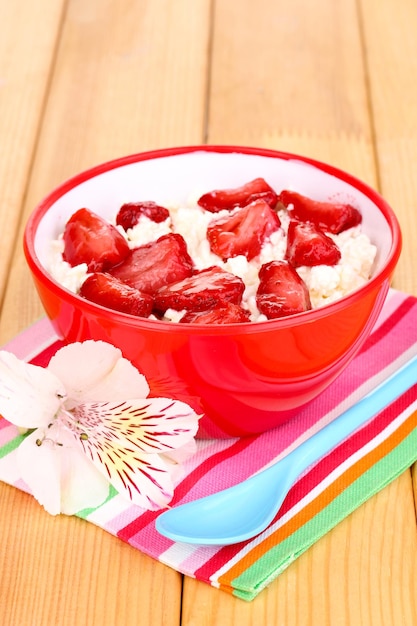 나무 테이블에 얇게 썬 딸기가 있는 빨간 그릇에 코티지 치즈