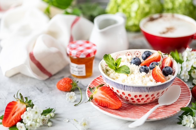 Cottage cheese with berries, jam, fresh strawberries and a cup of coffee with cream for breakfast.