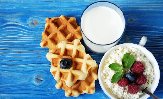 Cottage cheese with berries waffles and milk on a wooden blue b