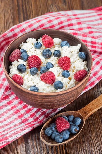 Cottage cheese with raspberries and blueberries in brown clay bowl