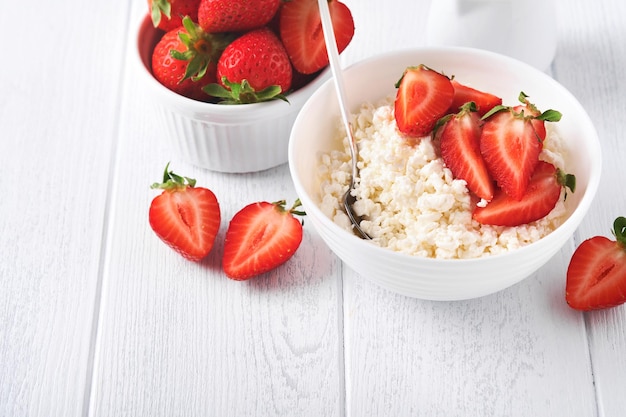 Cottage cheese with strawberries Breakfast from cottage cheese with slices fresh strawberries cream cup of coffee in white bowl on white wooden background Top view Food concept Mock up