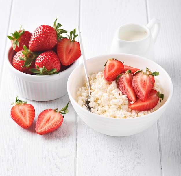 Cottage cheese with strawberries Breakfast from cottage cheese with slices fresh strawberries cream cup of coffee in white bowl on white wooden background Top view Food concept Mock up