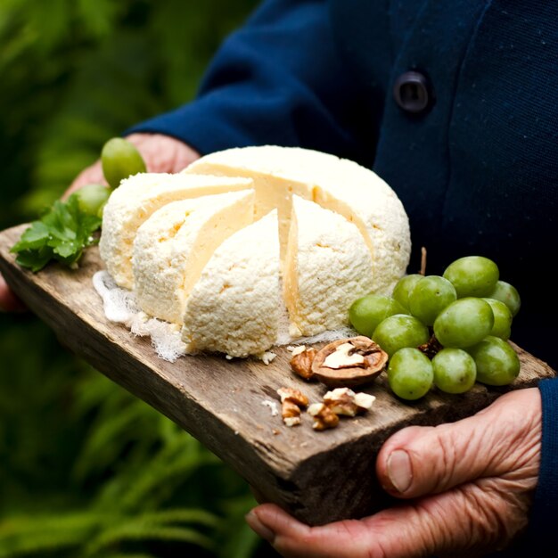 Cottage cheese on a wooden tray, with grapes, a walnut, in hands of the elderly woman