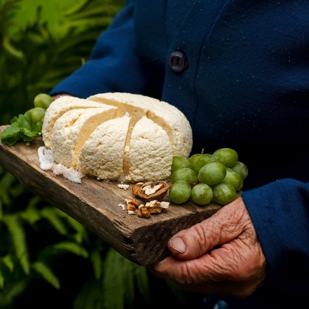 Cottage cheese on a wooden tray, with grapes, a walnut, in hands of the elderly woman