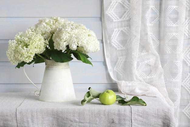 Photo cottage still life with a bouquet of hydrangeas in a tin bucket and a green apple on the table