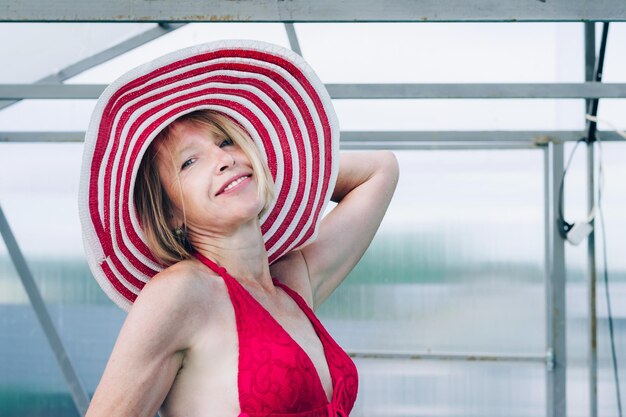 Cottagecore and Staycation at home. Happy elderly blonde woman in swimsuit and hat. Indoor home pool. Relax in isolation.