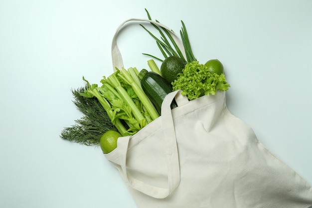 Cotton bag with green vegetables on white background