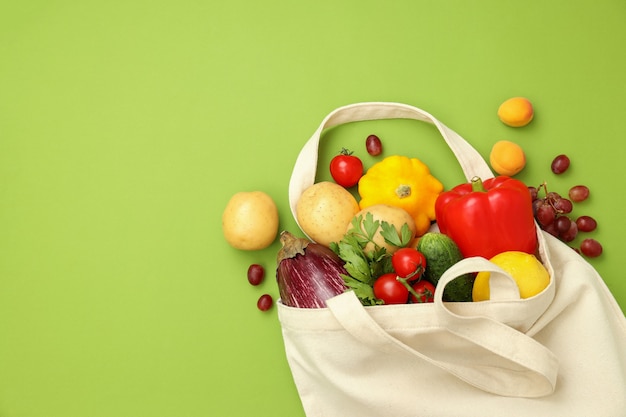 Cotton bag with vegetables and fruits on green background