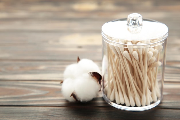 Cotton buds in container with cotton flower on wooden brown background