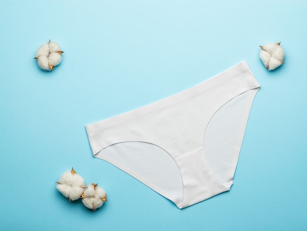 Cotton buds and white women's panties on a light blue background. Lingerie. Flat lay.