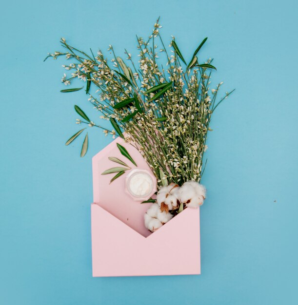 Cotton and cream with herbs in pink envelope on blue background. Above view