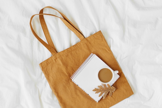 Cotton eco bag with cup of coffee on bed. Autumn concept.