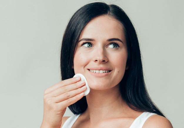 Il viso della donna del batuffolo di cotone rimuove il trucco naturale della pelle sana. colpo dello studio.