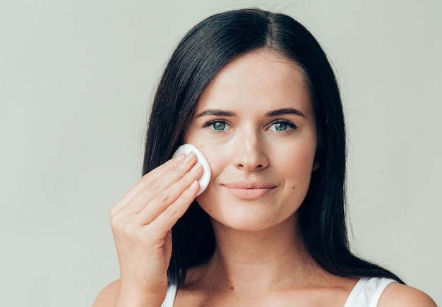 Il viso della donna del batuffolo di cotone rimuove il trucco naturale della pelle sana. colpo dello studio.