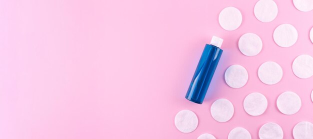 Ватные подушечки синяя бутылка с тонером или мицеллярной очищающей водой на розовом фоне вид сверху