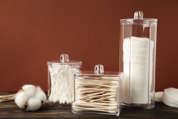 Cotton pads and cotton sticks in containers with cotton flower on brown background