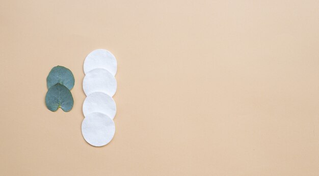 Cotton pads and fresh eucalyptus leaves on a beige background. Flat lay, top view, copy space. Women's health care