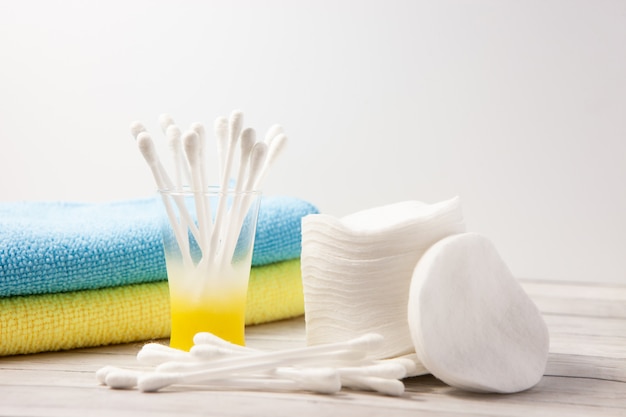 Cotton pads and sticks in a glass on a light background, next to a blue and yellow towel