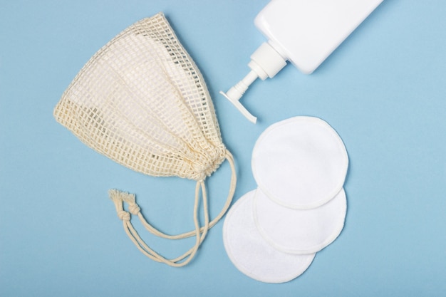 Cotton reusable make-up remover pads in a cloth bag and face wash and cleanser on a blue background. The concept of ecology and conscious consumption. Reusable cotton pads