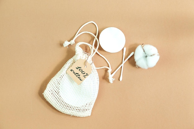 Cotton reusable makeup remover pads in a fabric bag and a ball of cotton on a beige background