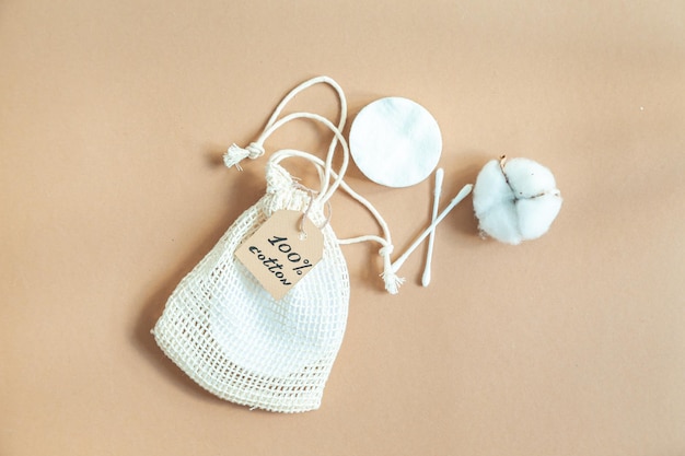 Cotton reusable makeup remover pads in a fabric bag and a ball of cotton on a beige background